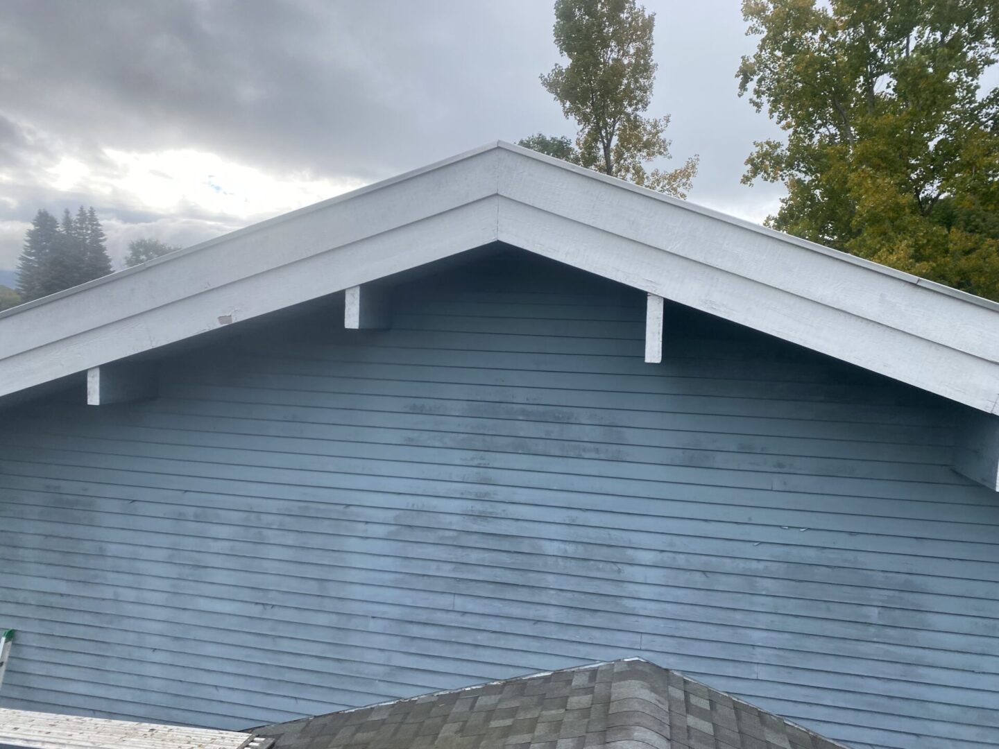 Blue house exterior with white roof trim under cloudy sky.
